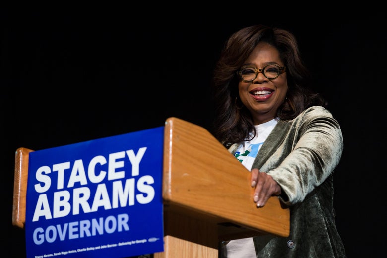 Oprah stands behind a podium with a Stacey Abrams sign on it.
